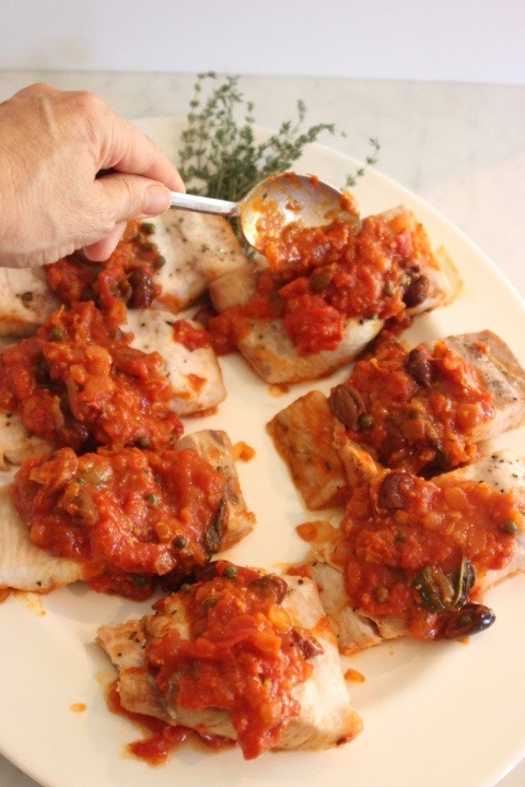 Baked FIsh with red tomato sauce with olive and herbs being spooned over it