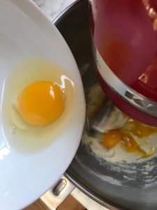Egg being added to a mixer bowl with butter and sugar