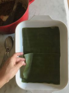 Partially cooked green pasta laid out on the bottom of a rectangular baking pan