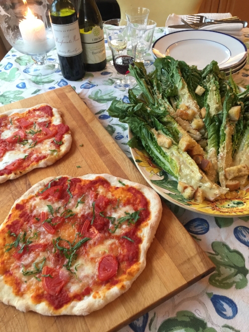 Baked pizzas on a wooden cutting board with classic caesar salad in a serving bowl