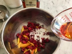 mixing bowl with raspberries and peaches with liquor being poured on top