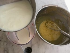 warmed milk being poured into a measuring cup, bowl with beaten egg yolks