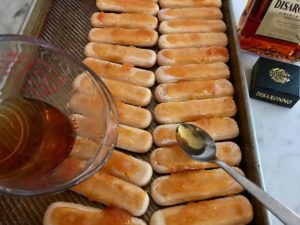 apricot jam and amaretto being placed on the lady fingers