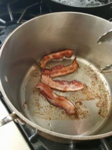 Bacon being cooked in the bottom of a pan