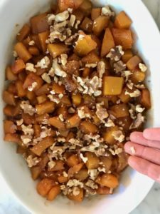 butternut squash in a baking dish being sprinkled with nuts