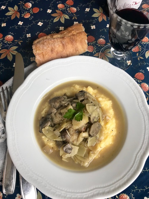 chicken with artichokes and mushrooms on a white plate with polenta