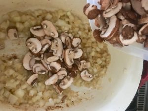 dutch oven with cooked onions and mushrooms being added