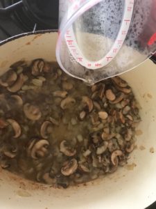 adding wine to the dutch oven with the mushrooms and onions