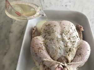 chicken on top of the onions in a baking dish with wine being added to the dish