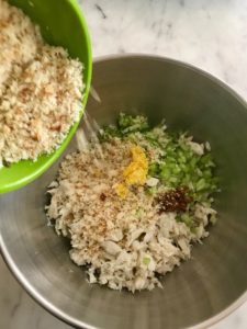 crab meat, herbs, and breadcrumbs being added to the mixing bowl