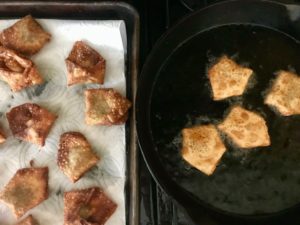 saute pan with wontons being fried and a baking sheet with finished wontons