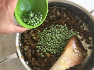 cooked ground beef with frozen peas being added