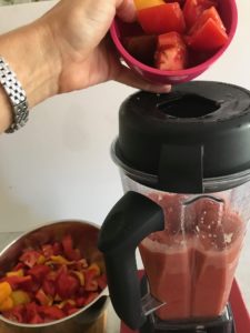 vitamix blender with tomatoes being added to it