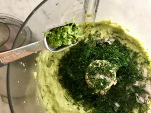 avocado mixture in food processor with herbs being added
