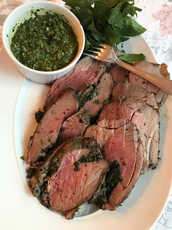 Herb crusted leg of lamb on a serving platter with a side of mint salsa verde