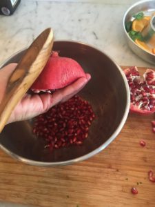 wooden spoon tapping on pomegranate half to remove seeds