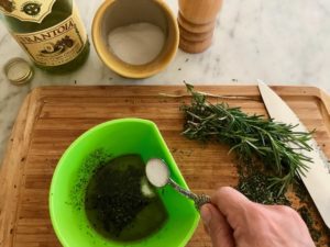small bowl with olive oil and herbs with salt being added