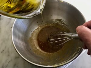 bowl with vinaigrette and olive oil being poured in