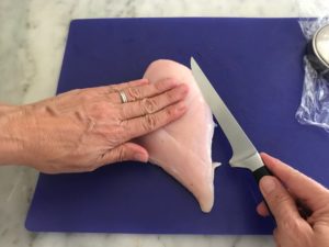 chicken breast on a cutting board with hand flat on top