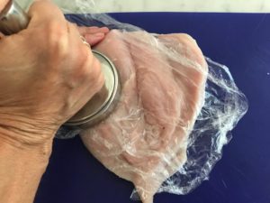 chicken with plastic wrap over it being pounded out