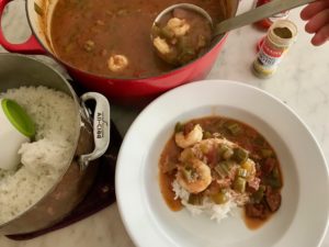 Pouring gumbo over white rice in a serving dish