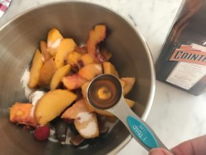 fruit in a mixing bowl with sugar and liquor being added
