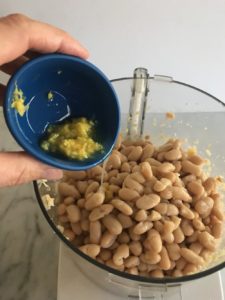 beans and garlic mixture in food processor with lemon zest being added
