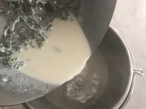 saucepan with herbs and heavy cream being strained