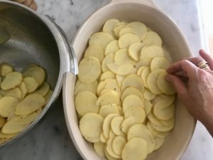 potato slices being layered into a baking dish