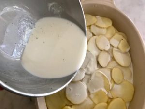 pouring the milk mixture over the potatoes in the baking dish