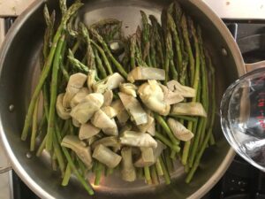saute pan with asparagus and artichokes in it