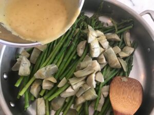 drizzling the vinegar sauce over the asparagus and artichokes