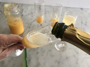 glasses with peach mixture and sparkling wine being poured in