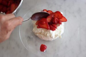finished meringue on a plate being topped with strawberries
