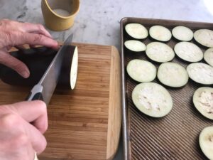 sliced eggplant being placed on a baking sheet