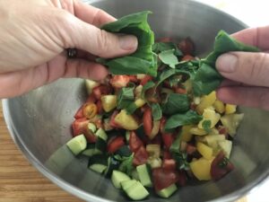 tearing basil and adding it to the bowl with tomatoes and cucumbers