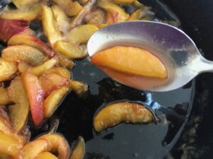 cooked peaches in a skillet and one peach slice on a spoon
