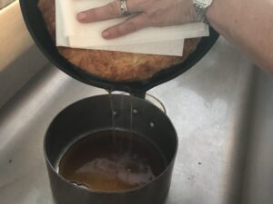 pouring the juice out of the pan using a paper towel and your hand to hold the tart in
