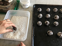 A tray of round dough balls with one being rolled in a container of large grain sugar.