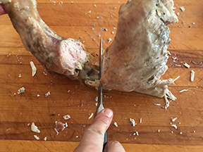 A knife cutting turkey to separate the leg and thigh.