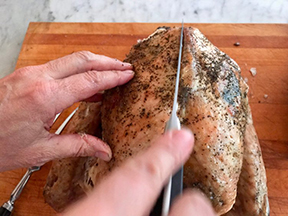 A knife cutting down the center of the whole chicken