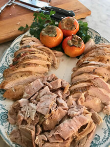 A platter filled with slices of turkey meat garnished with persimmons and herbs.